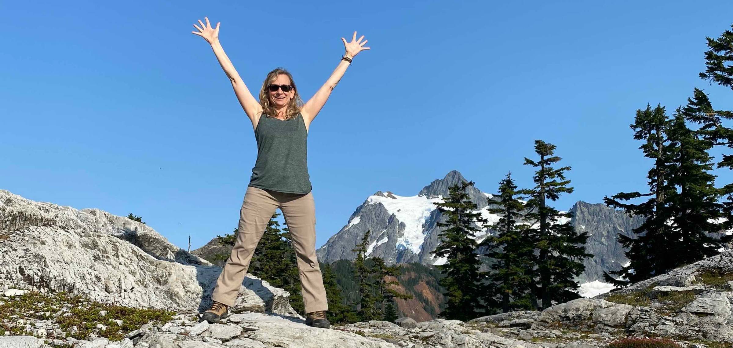 woman with arms open wide smiling on top of mountain