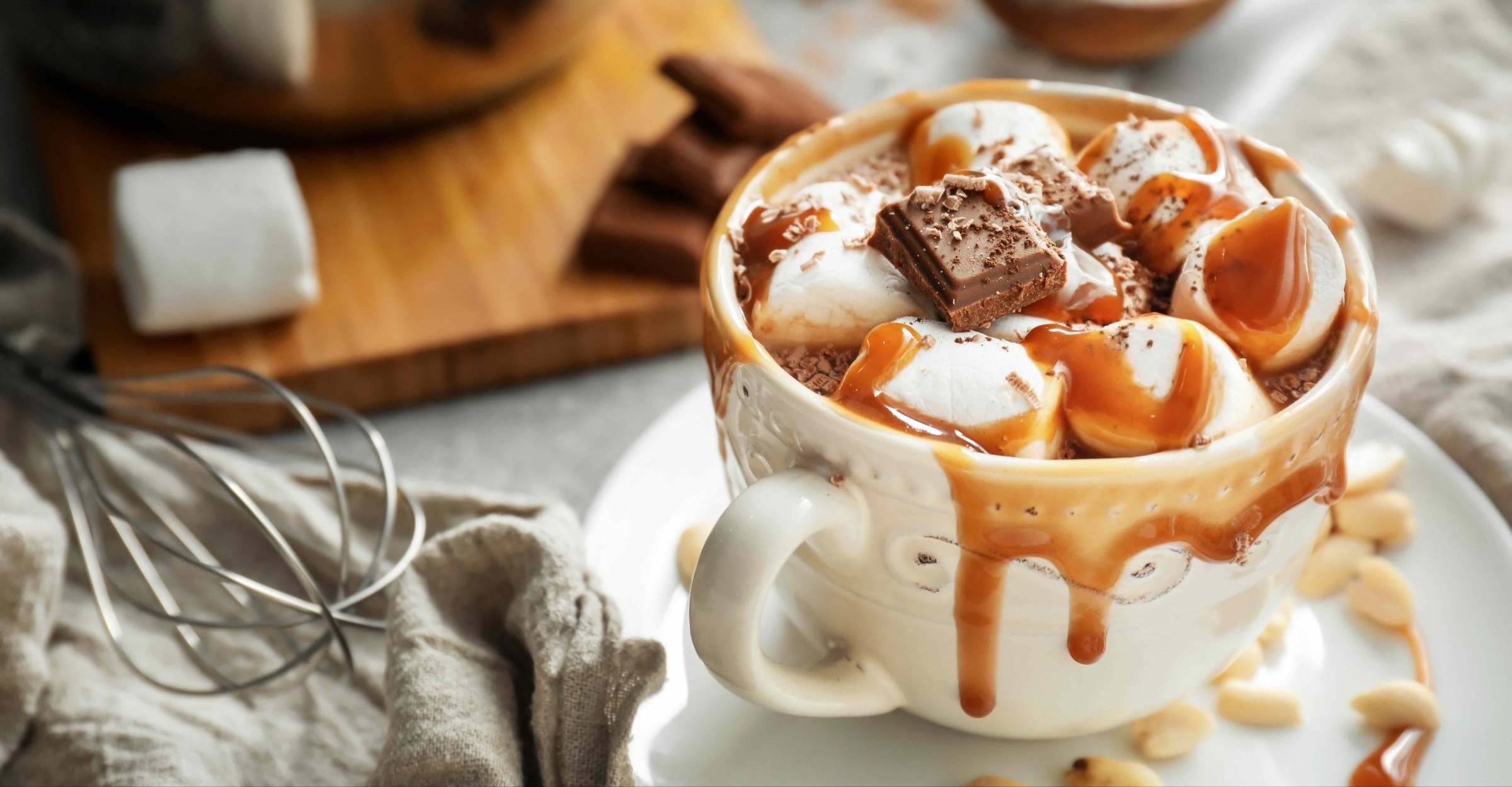 cup of hot cocoa with marshmallows a chunk of chocolate and caramel dripping over the sides