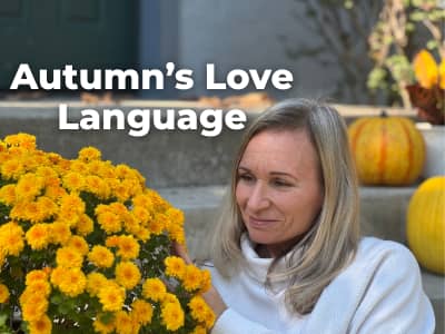 woman sitting on front steps looking closely at yellow mums