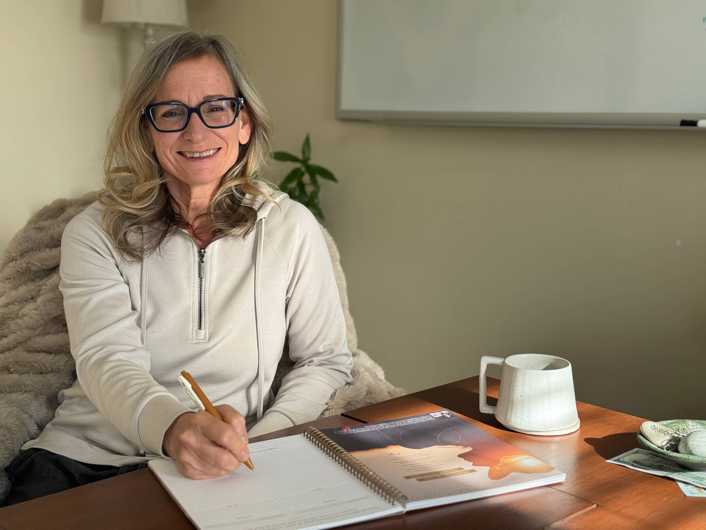 smiling woman sitting at desk with open journal and pen in hand