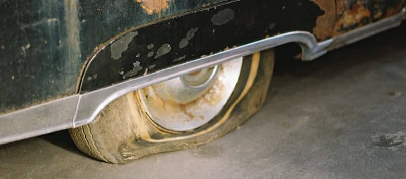 A flat tire on a rusted black car on a concrete floor