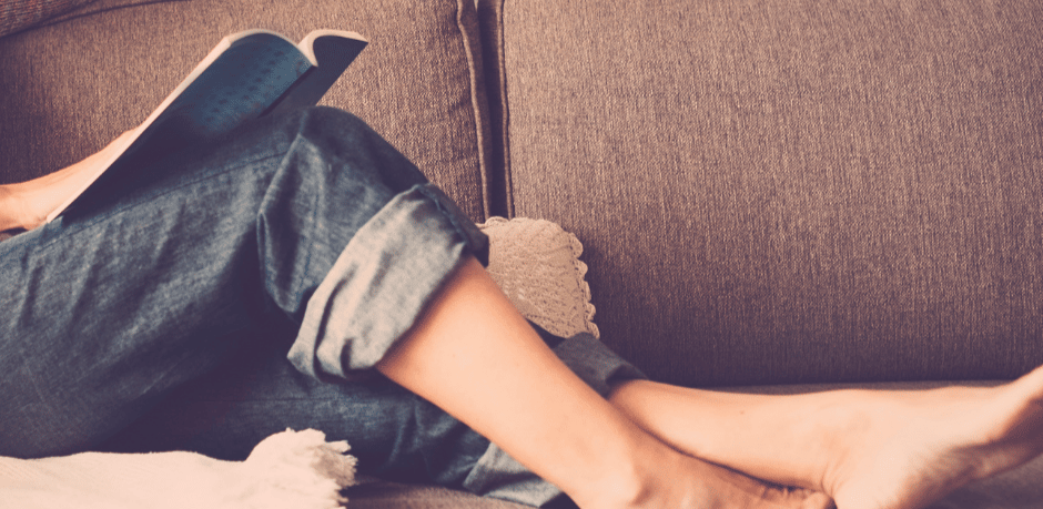 woman in blue jeans reading on a couch