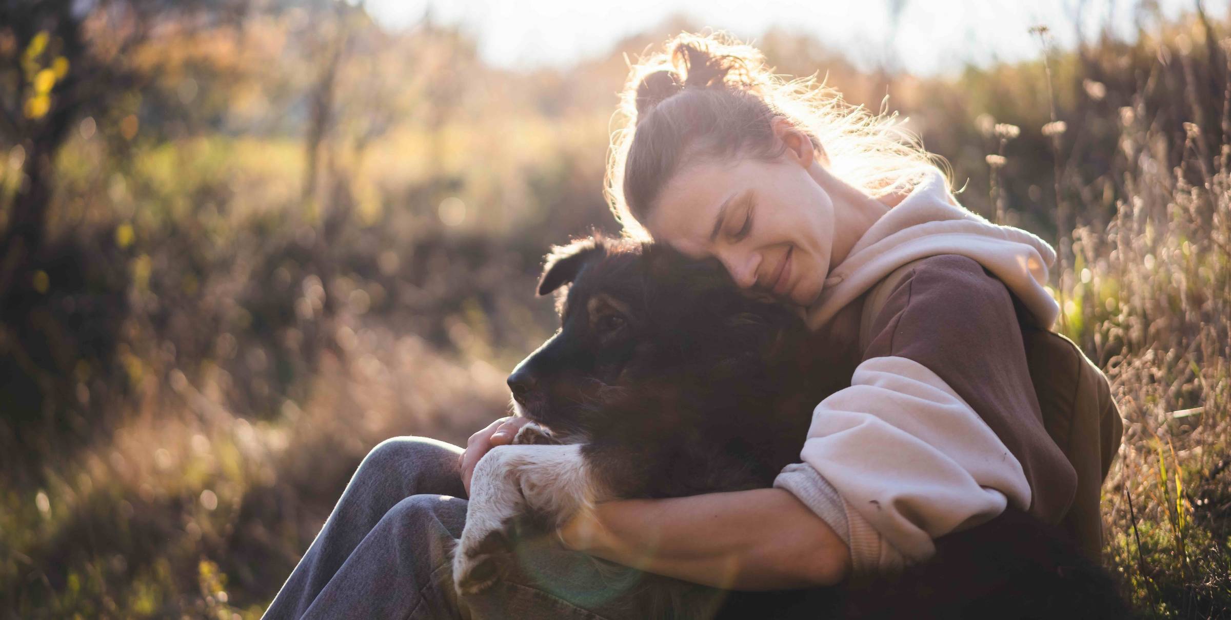 woman smiling hugging her dog in morning light