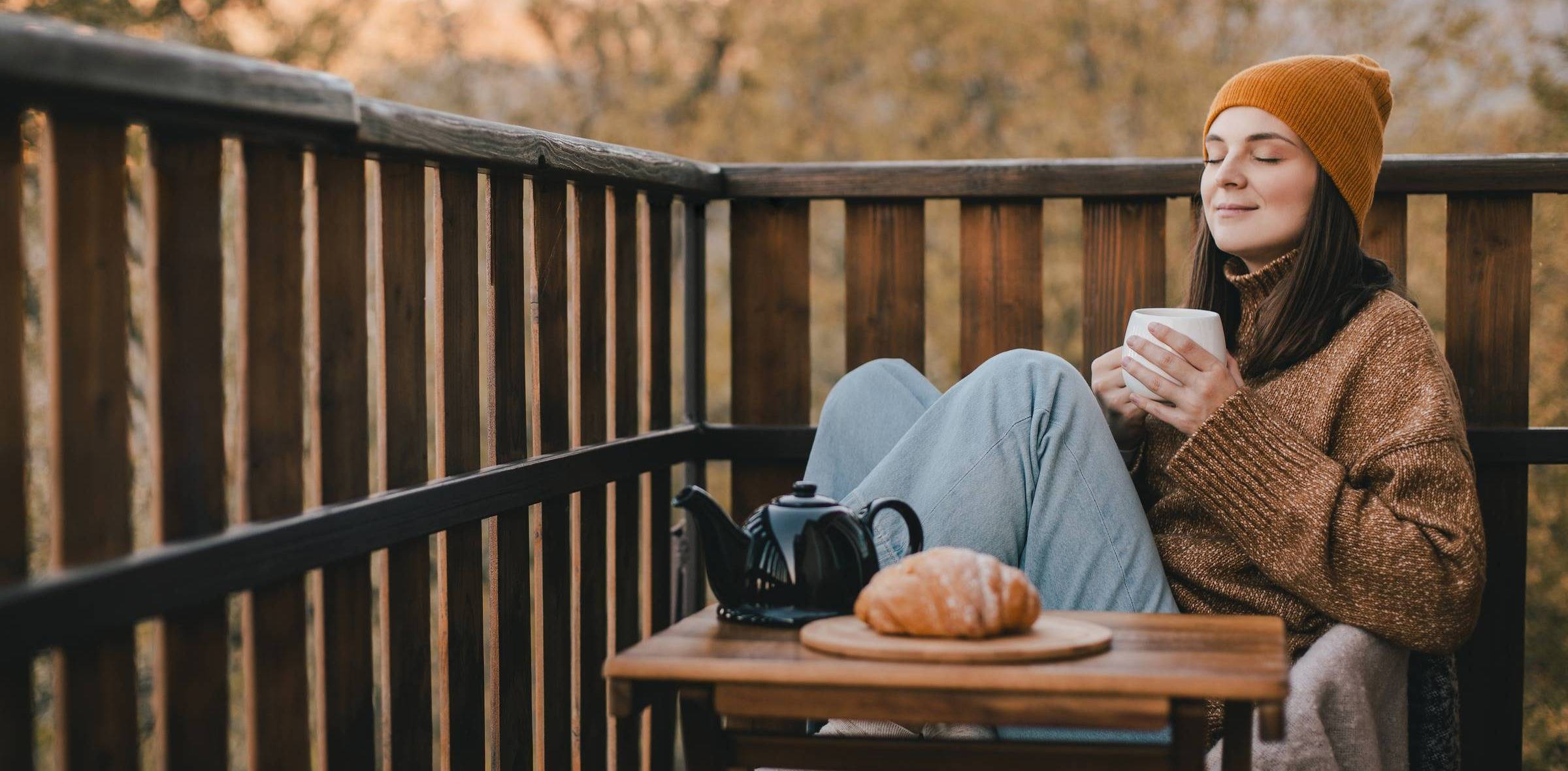woman in orange hat and blue jeans sitting on deck sipping a cup of tea