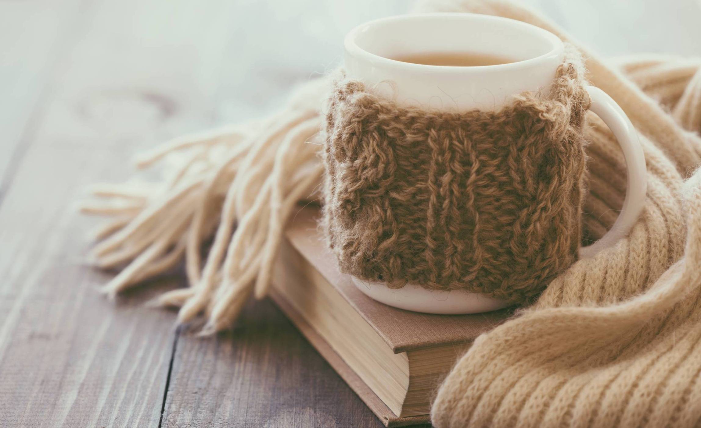 tan scarf and mug with a cozy tan knitted cup warmer around it on top of a book 