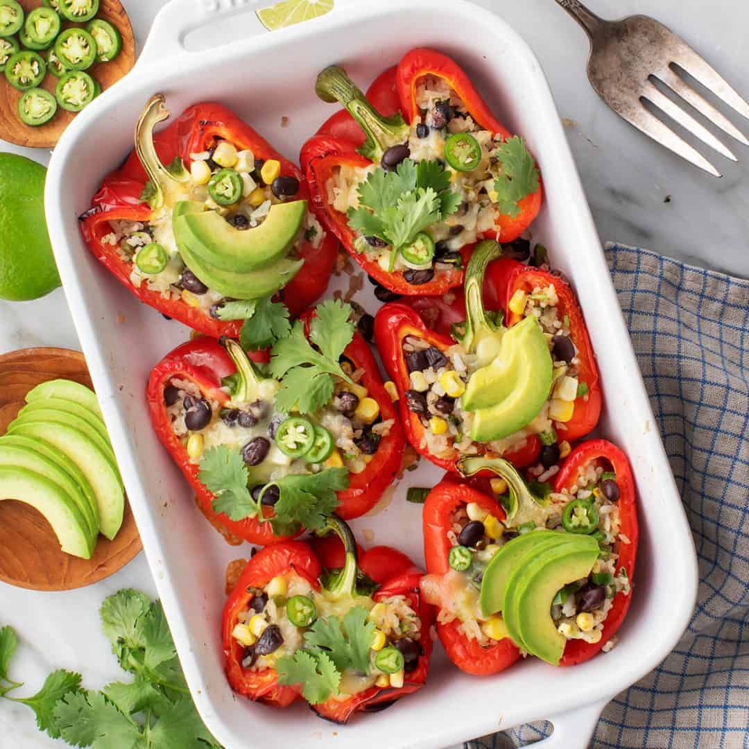 Cilantro lime rice-stuffed peppers in a baking dish with avocado and cilantro leaves