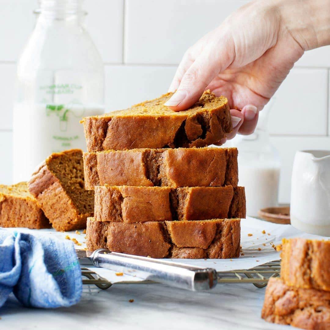 Hand picking up top piece from a stack of sliced pumpkin bread