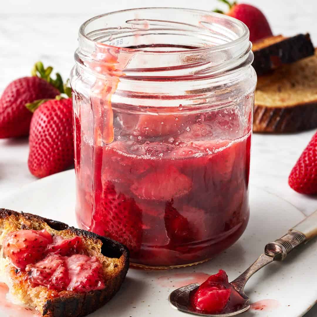 Jar of strawberry compote next to slice of toast