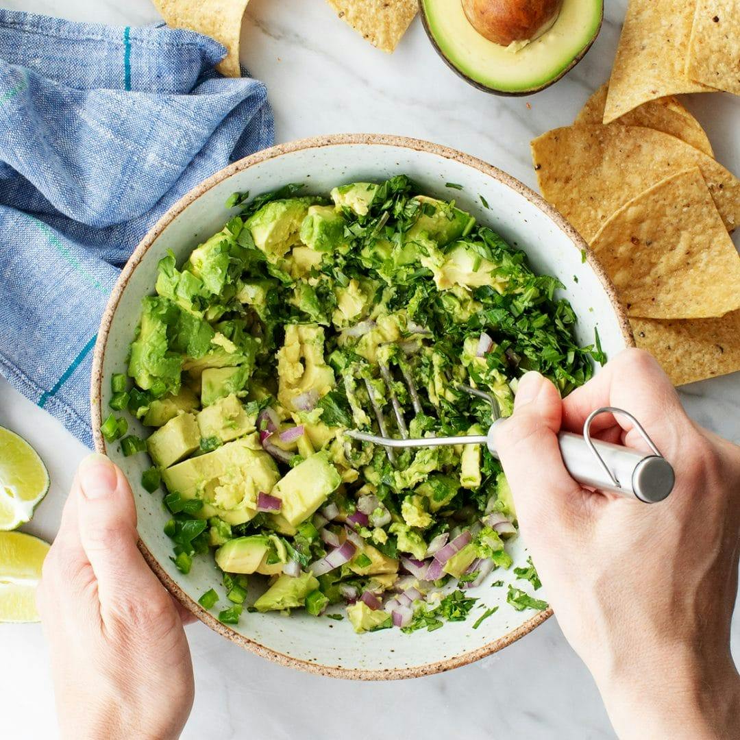 Hands mashing guacamole with a potato masher