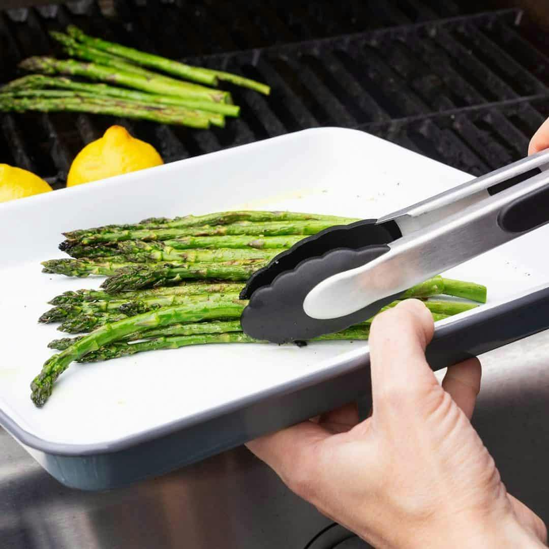 Tongs placing grilled asparagus on enamelware tray