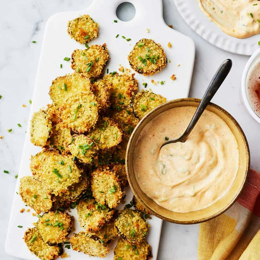 Air fryer fried pickles on a white serving board next to bowl of remoulade sauce