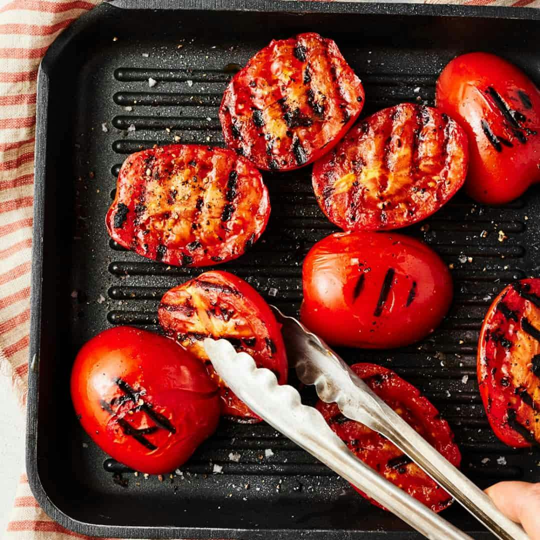 Hand using tongs to turn grilled tomato halves on a grill pan