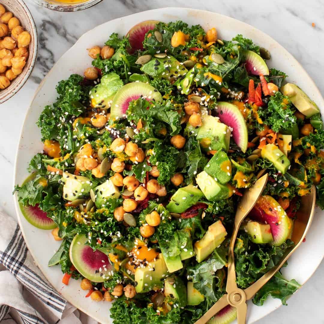 Kale salad on a plate with gold serving tongs