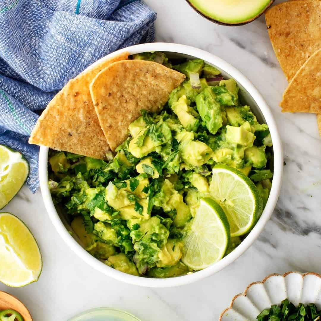 Bowl of guacamole with tortilla chips and lime wedges