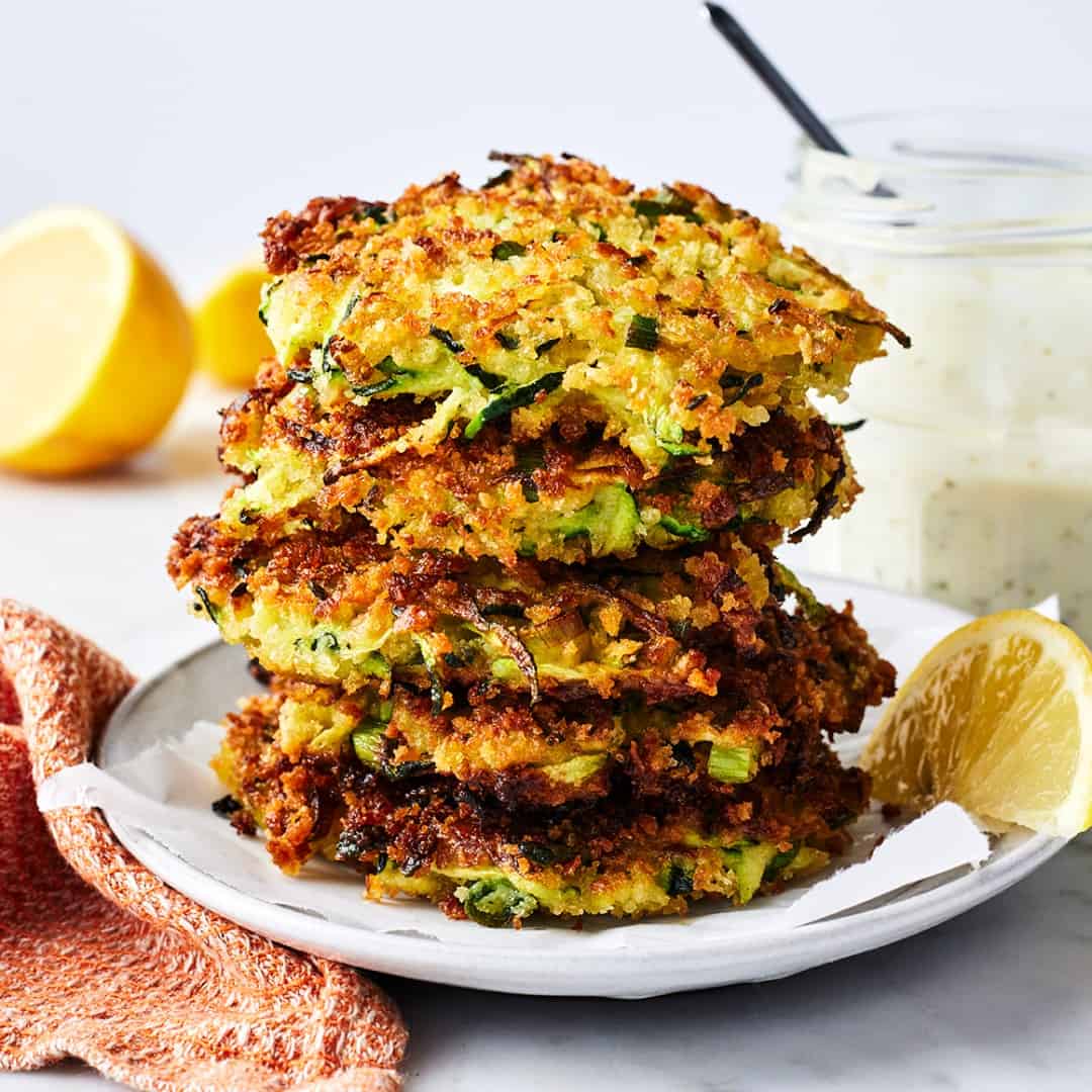 Stack of zucchini fritters on a plate with lemon wedge