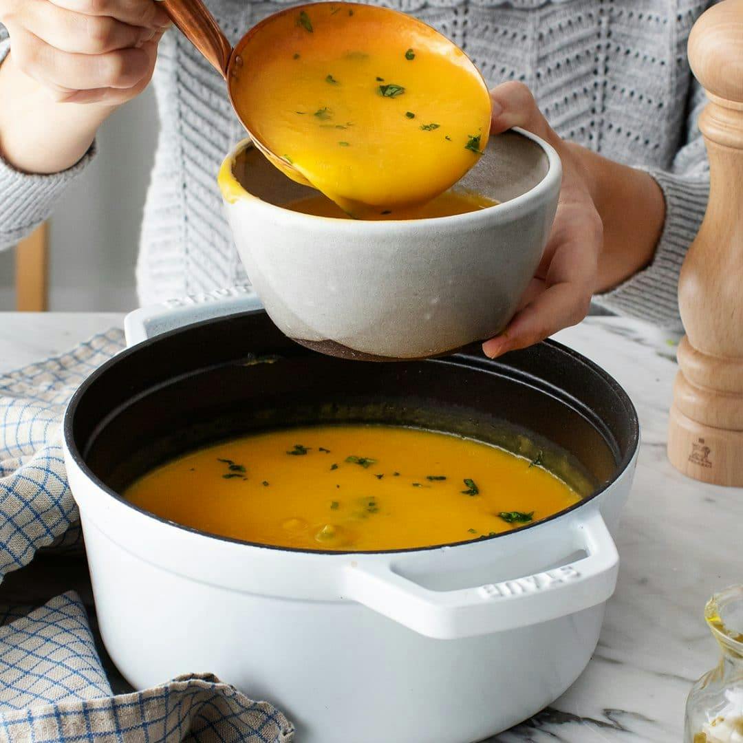 Hands ladling butternut squash soup into a bowl