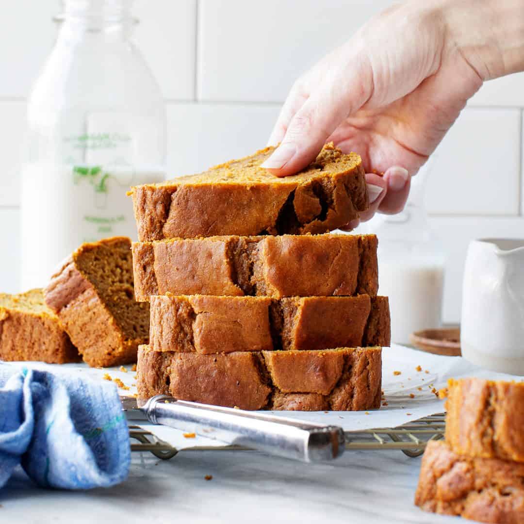 Hand lifting top slice off a stack of pumpkin bread slices