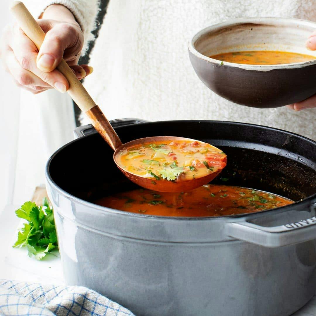 Hand with ladle scooping soup into bowl from pot