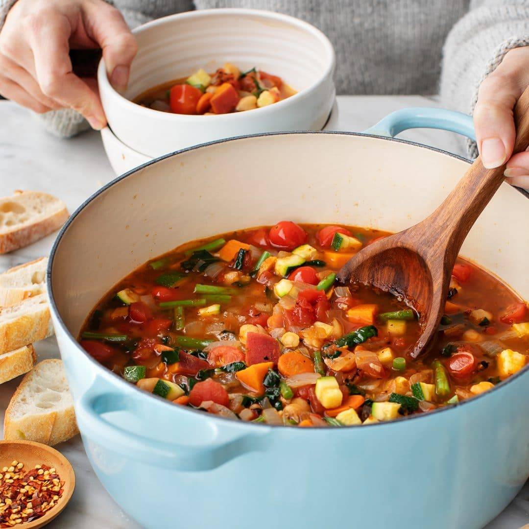 Hands using wooden ladle to scoop vegetable soup into bowls