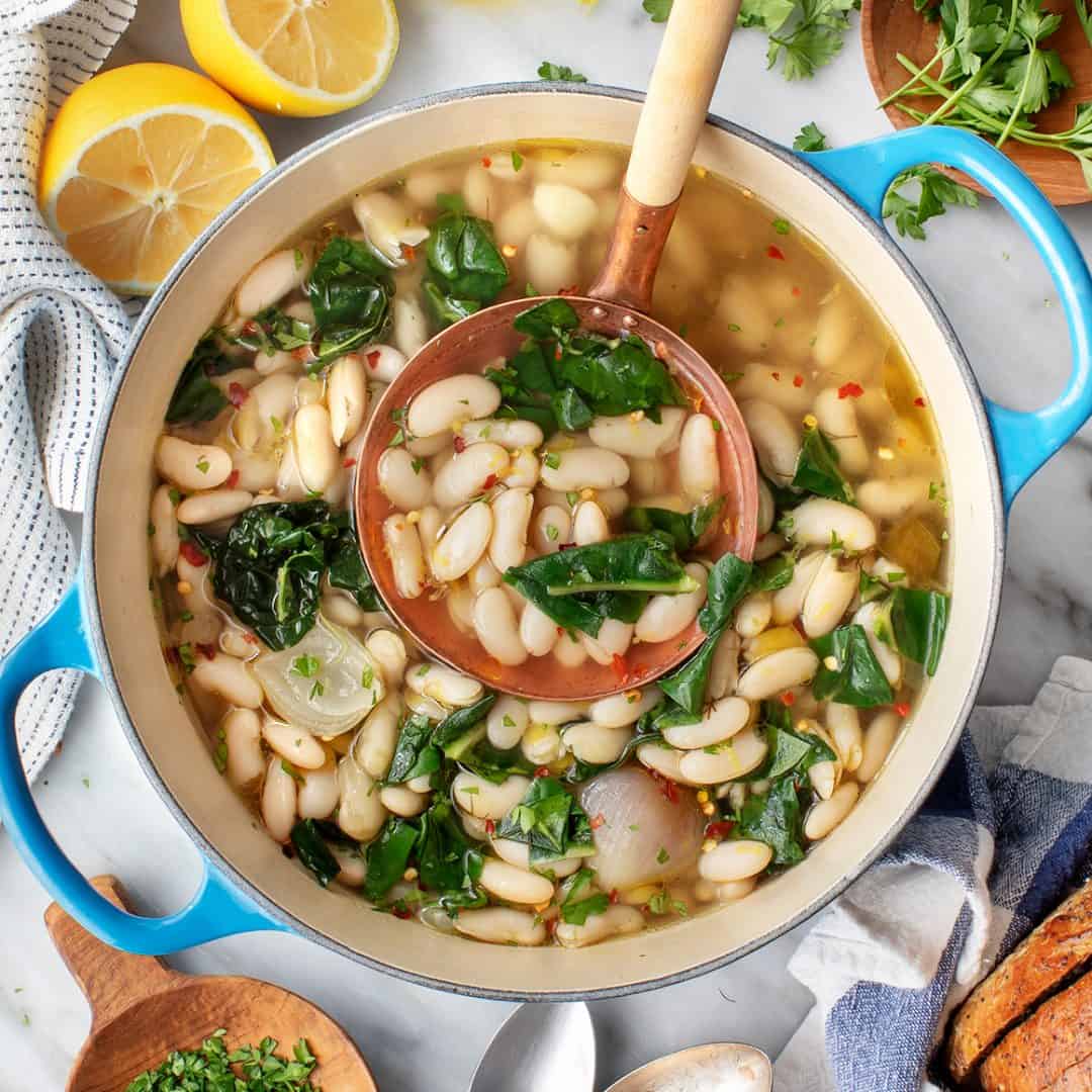 Brothy cannellini beans and greens in Dutch oven with copper ladle
