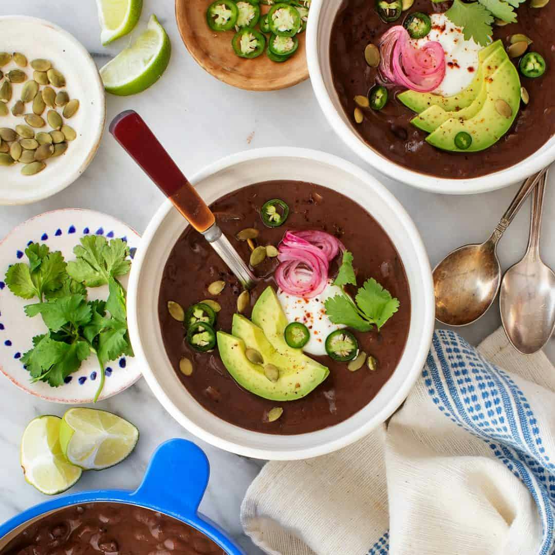 Black bean soup in bowls topped with avocado, pepitas, and pickled onions