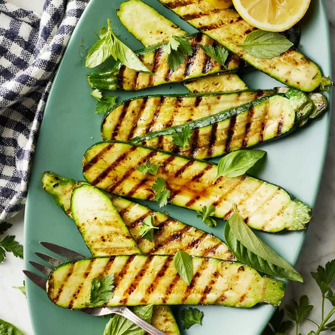 Grilled zucchini on a platter with parsley and basil