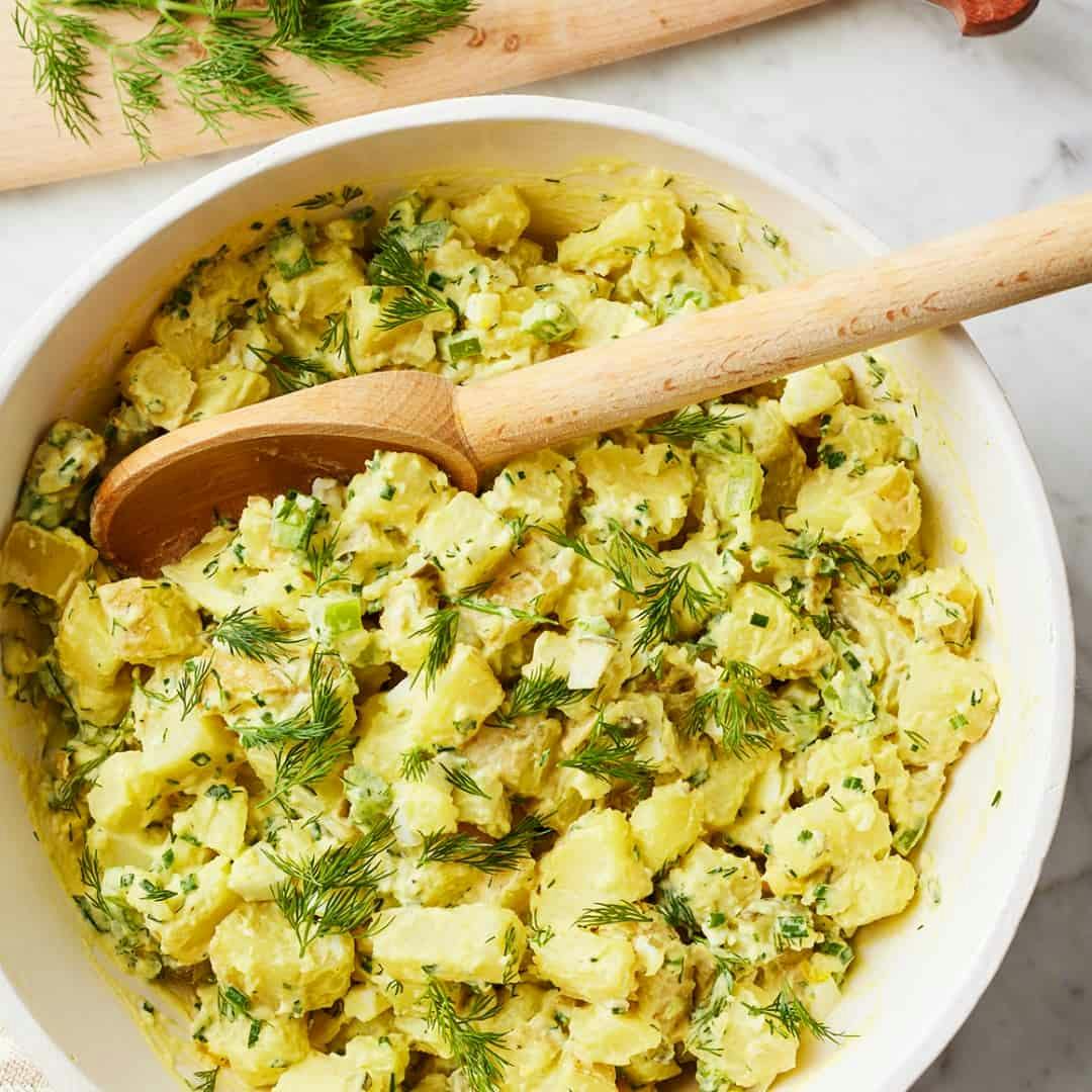 Bowl of creamy potato salad with wooden serving spoon