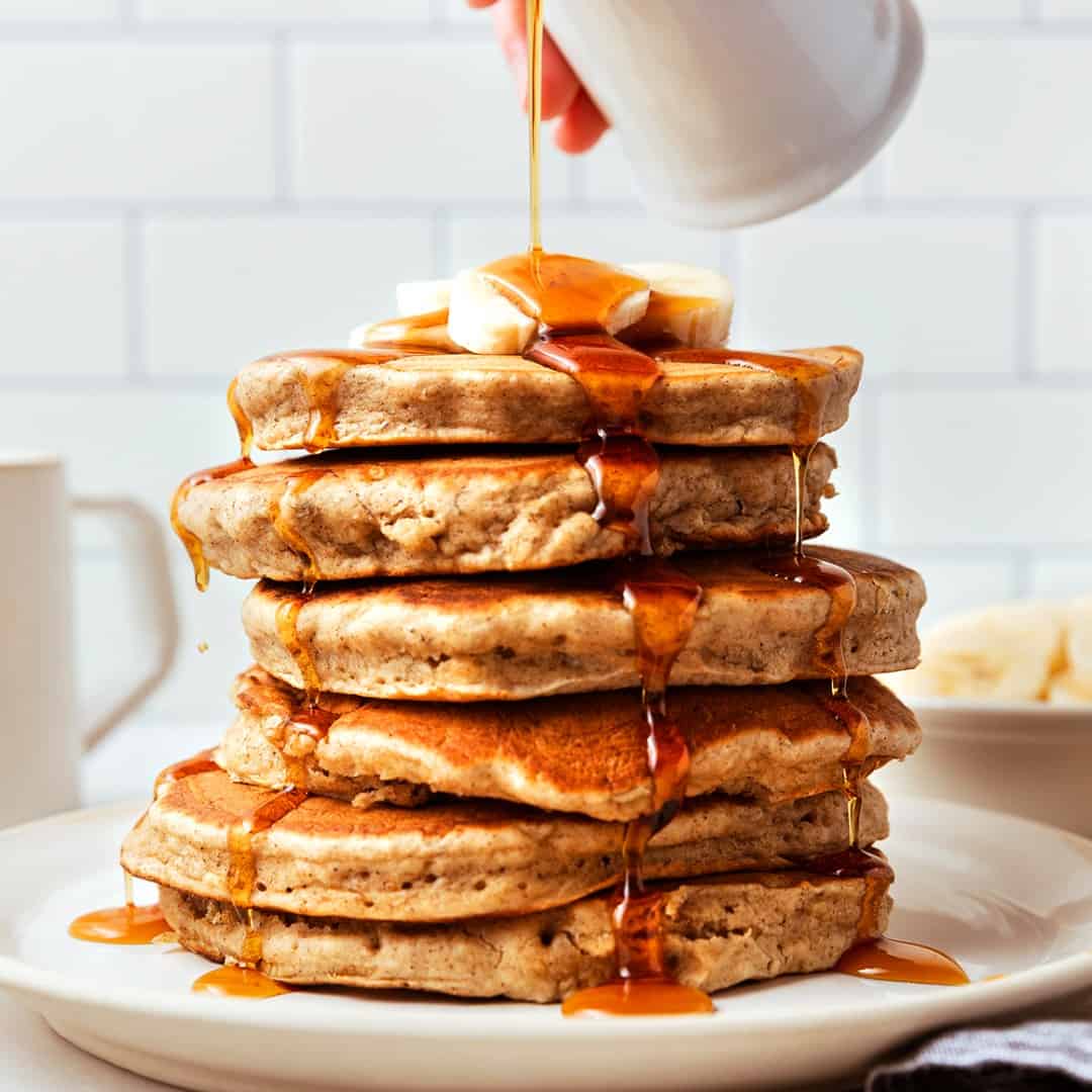 Stack of banana pancakes with maple syrup and sliced bananas