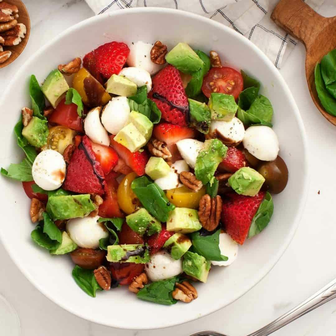 Strawberry salad with mozzarella, avocado, cherry tomatoes, basil, toasted pecans, and balsamic glaze in a bowl