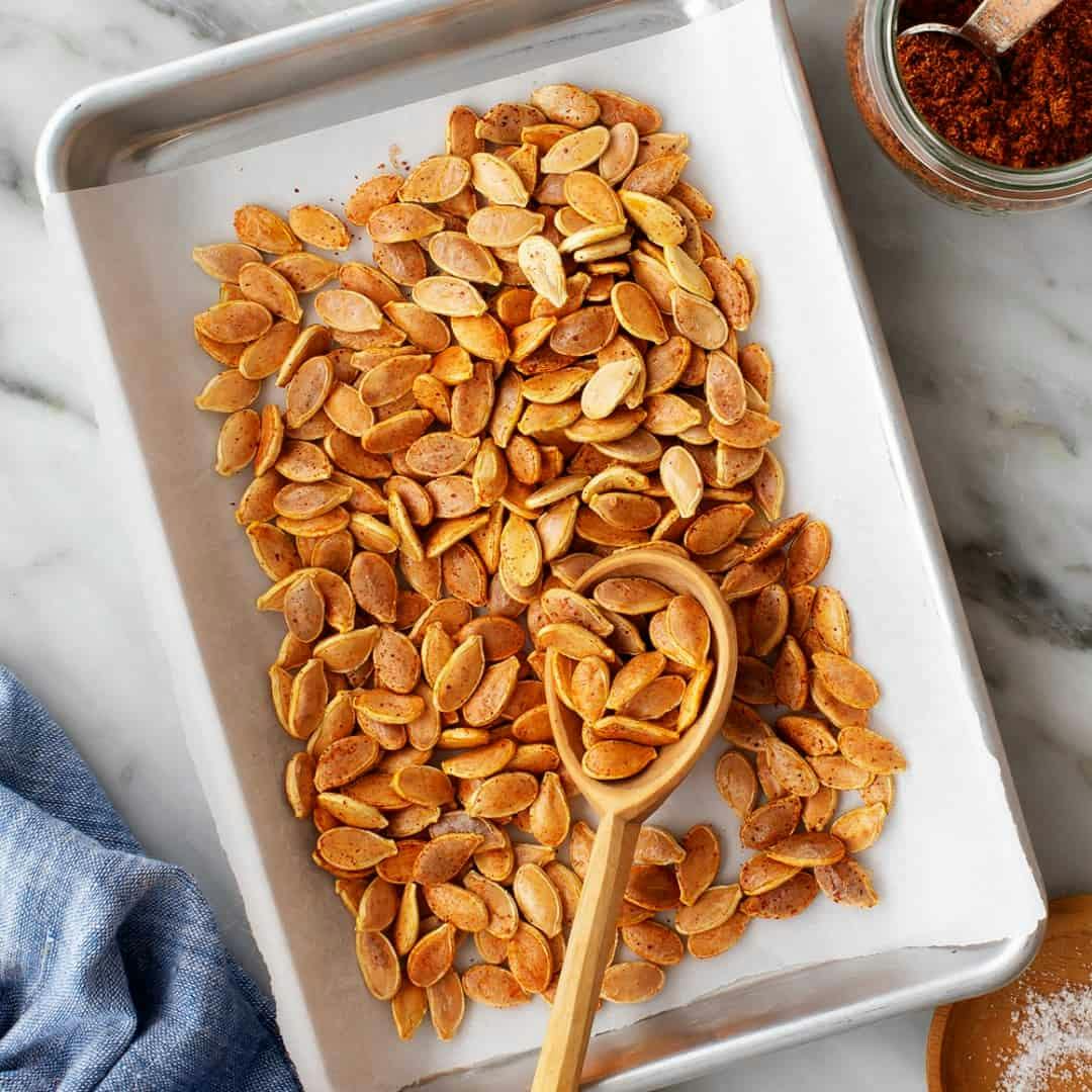 Roasted pumpkin seeds on a baking sheet with wooden spoon