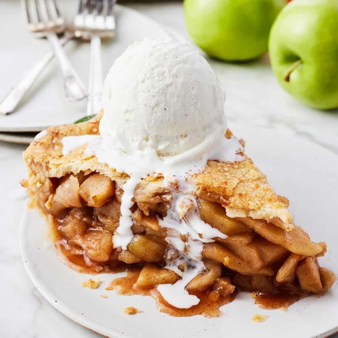 Slice of apple pie topped with vanilla ice cream on a plate