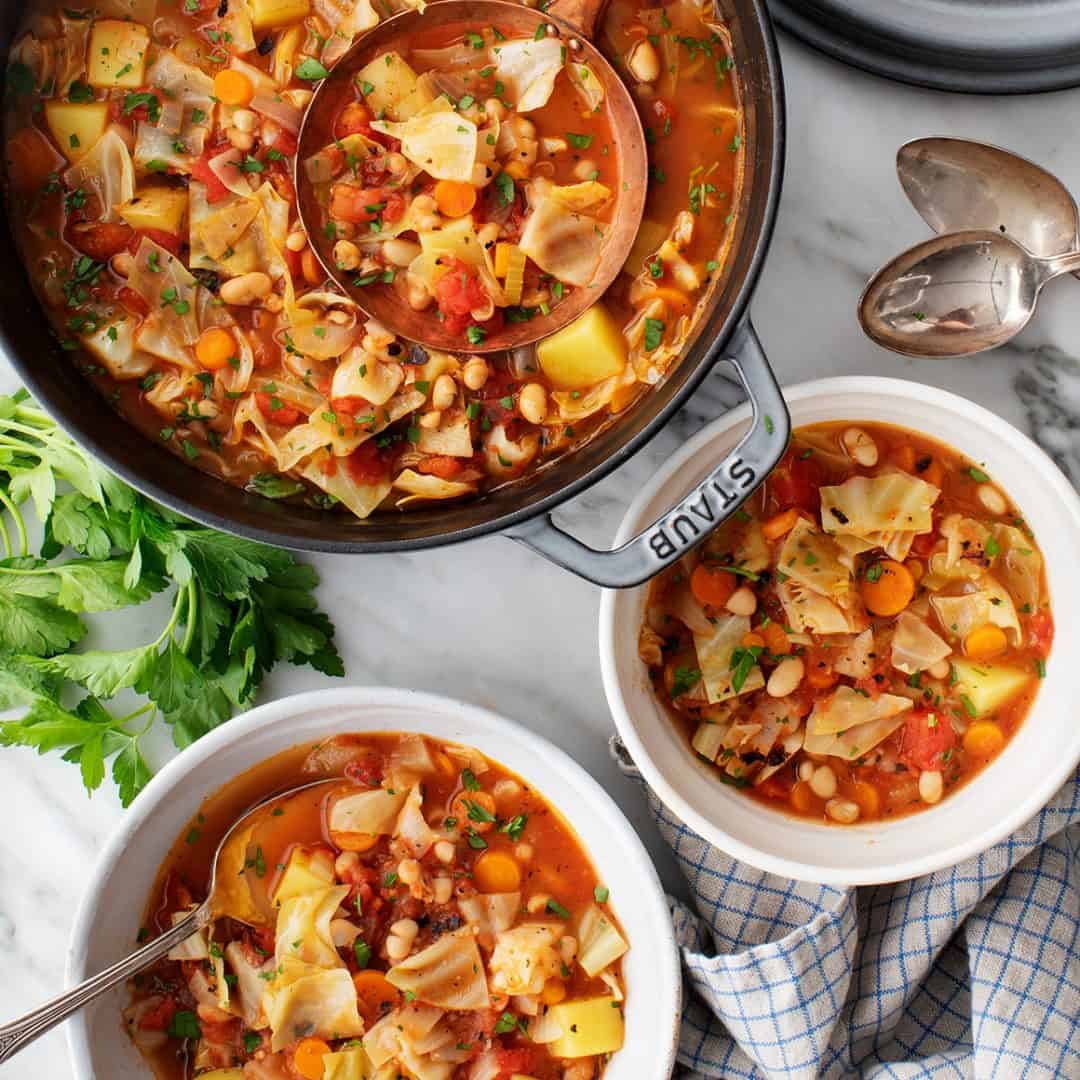 Pot of cabbage soup next to two bowls of cabbage soup