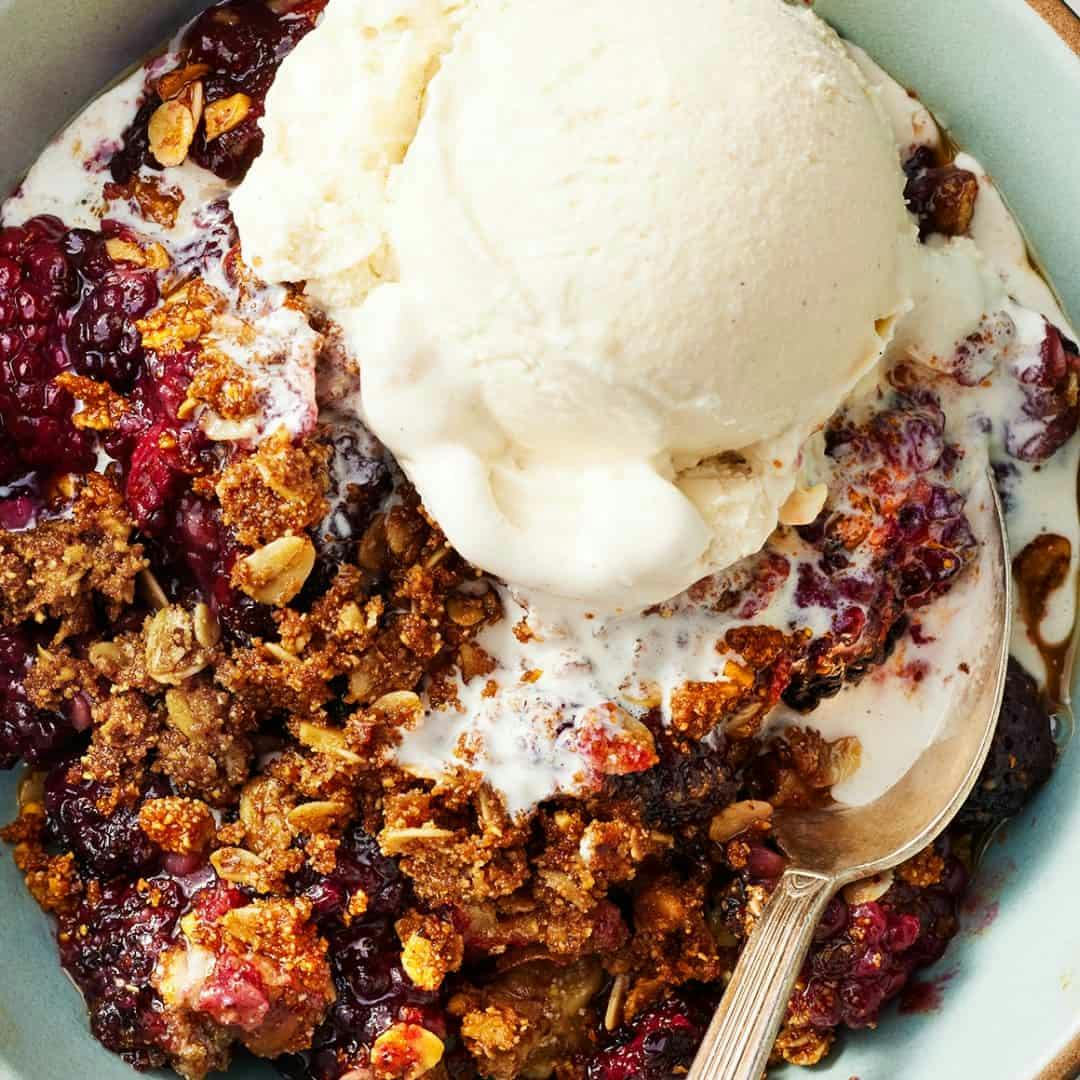 Blackberry crisp topped with vanilla ice cream in bowl with spoon