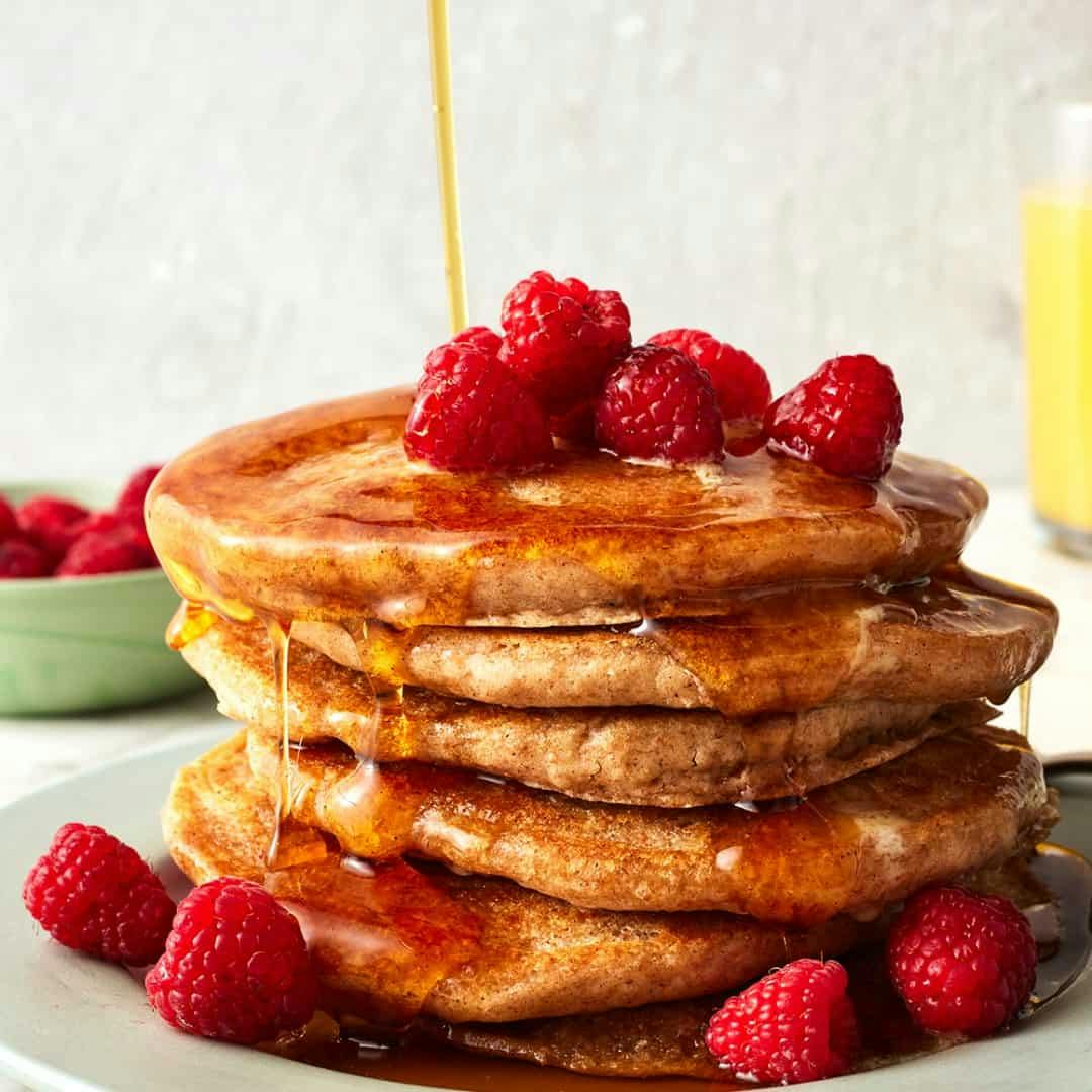 Stack of vegan pancakes topped with raspberries and maple syrup