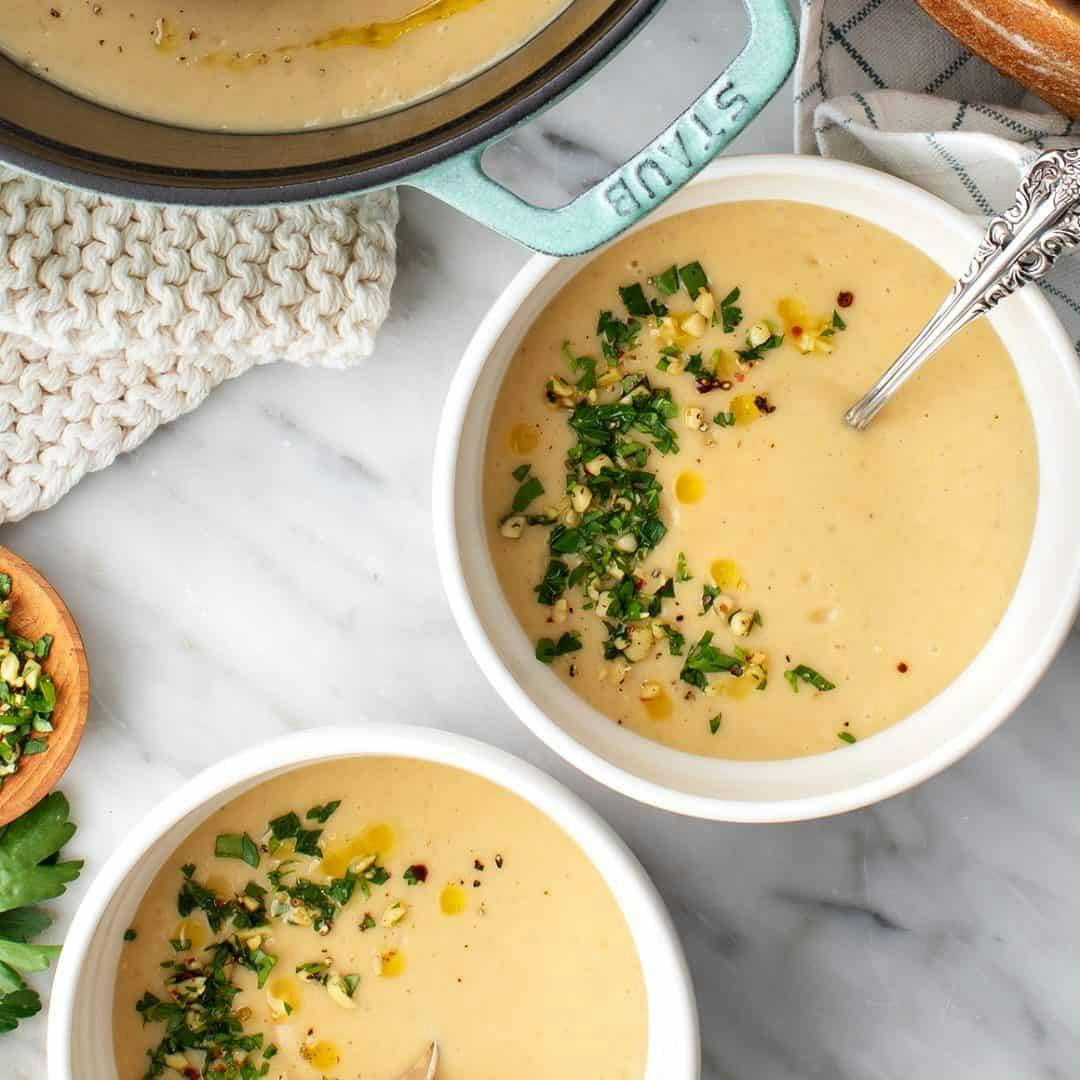 Two bowls of potato leek soup topped with parsley and pine nuts