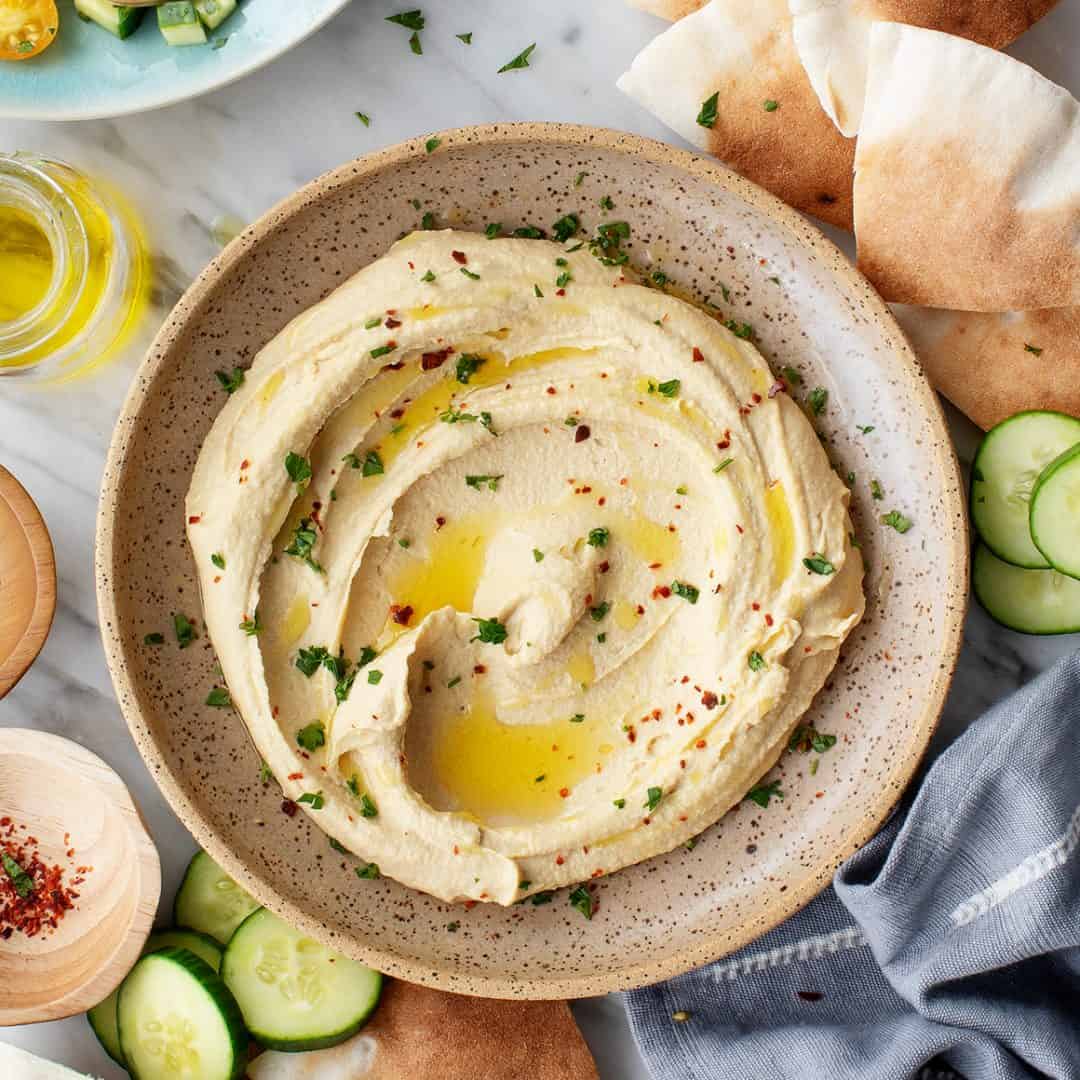 Bowl of hummus topped with olive oil, parsley, and red pepper flakes
