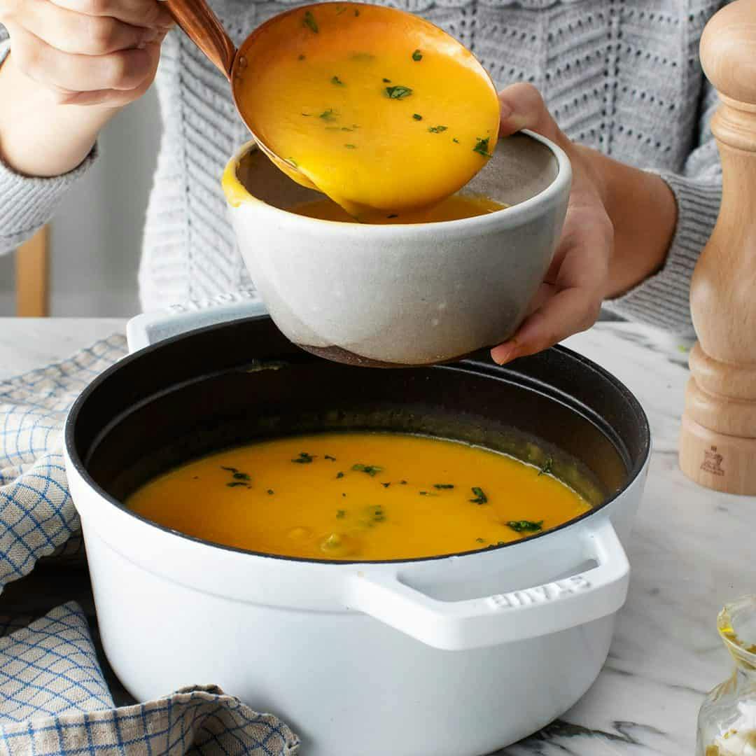 Hand ladling butternut squash soup from pot into bowl