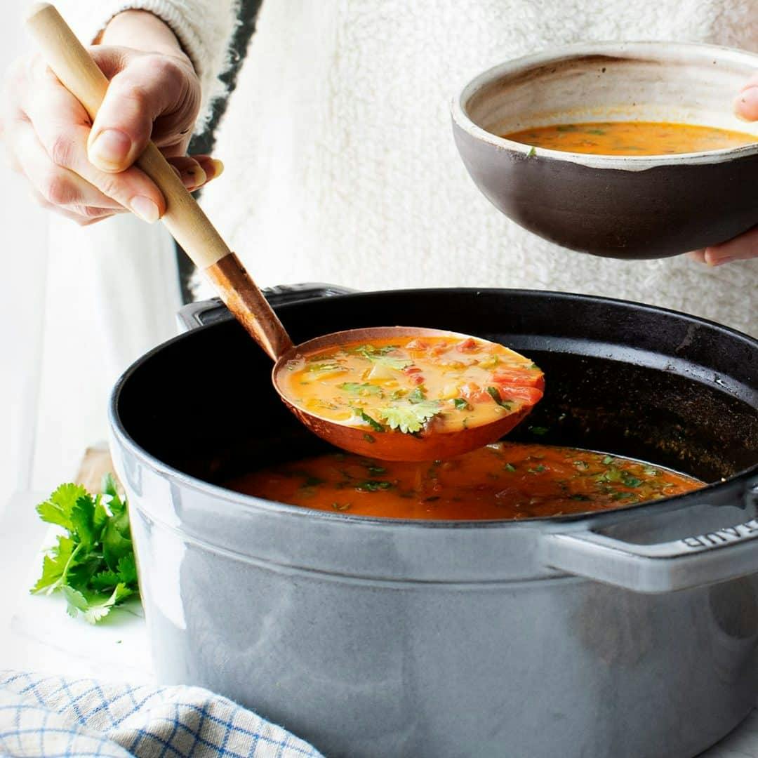 Hand ladling lentil soup from pot into bowl