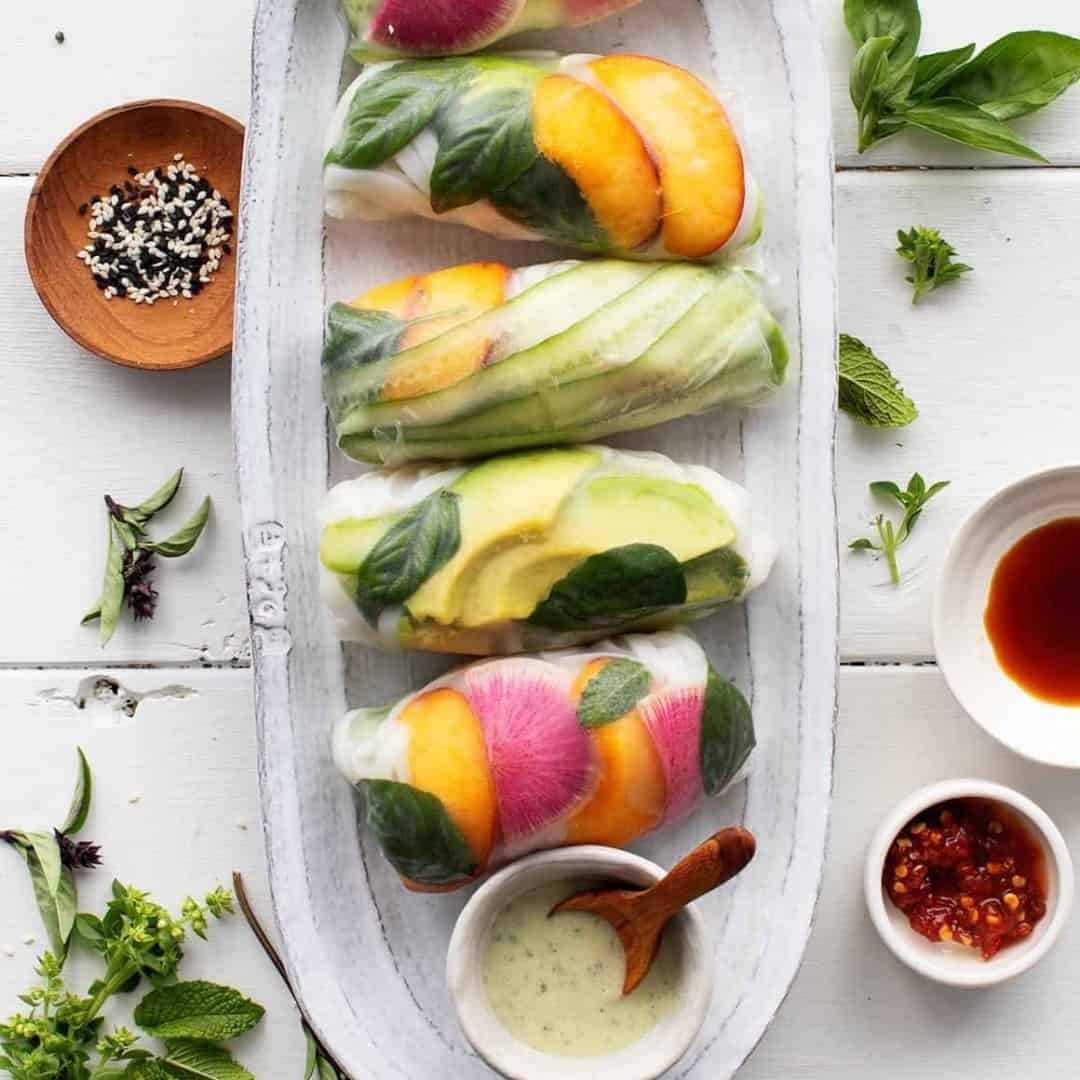Platter of peach, watermelon radish, cucumber, avocado, and basil summer rolls