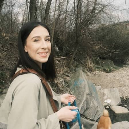 A woman smiles while walking a small dog outdoors.