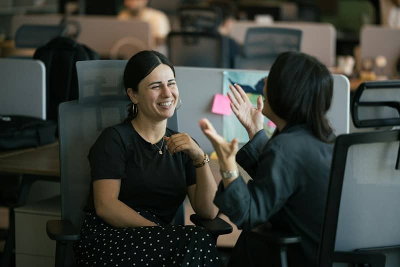 Two women laughing while talking in a modern office workspace