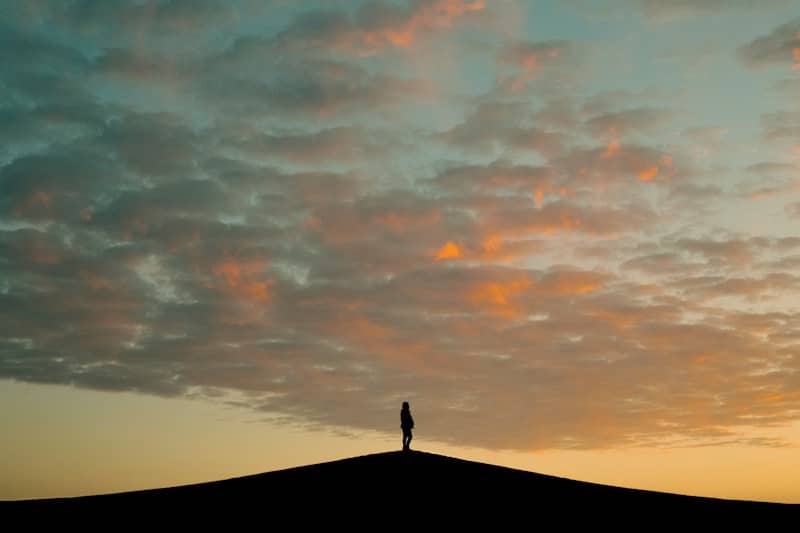 Silhouette of a person on a hill at sunset.