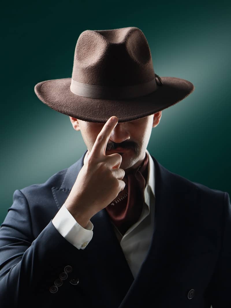 Man in fedora adjusts hat brim with finger.