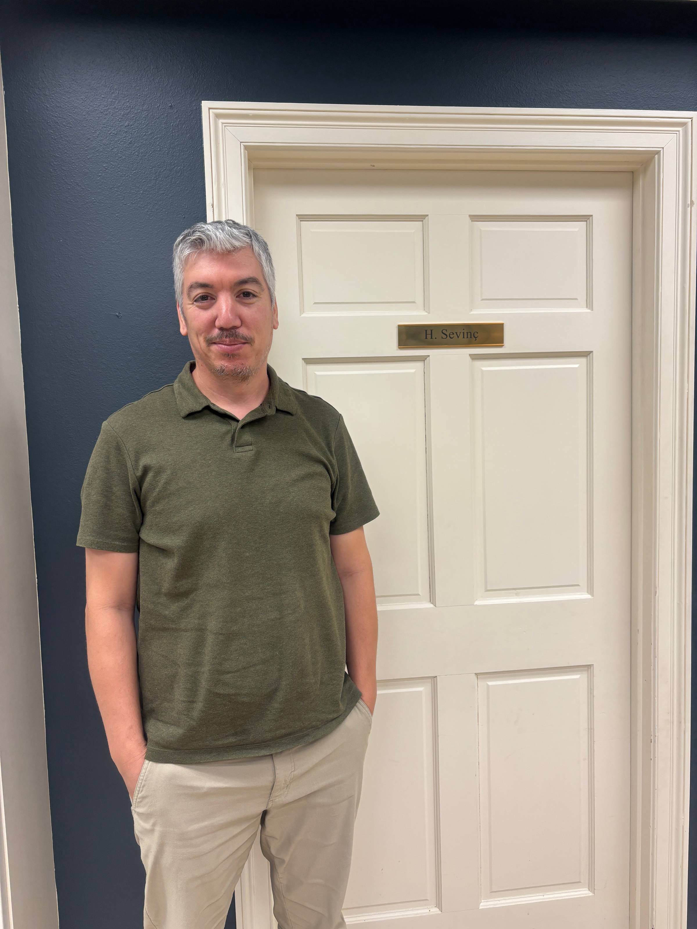 Hakan Sevinç standing in front of his office door nameplate at Kevin Harris Architect