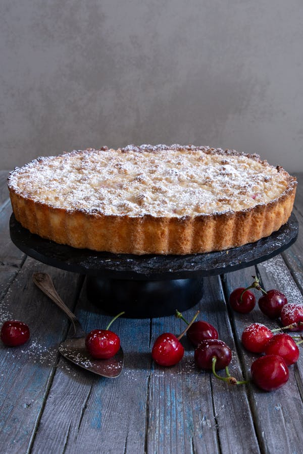 Cherry ricotta crumb cake on a black cake stand.