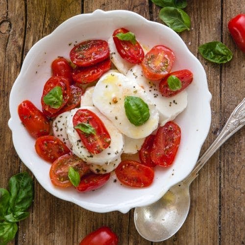 Caprese salad in a white plate with a silver spoon.