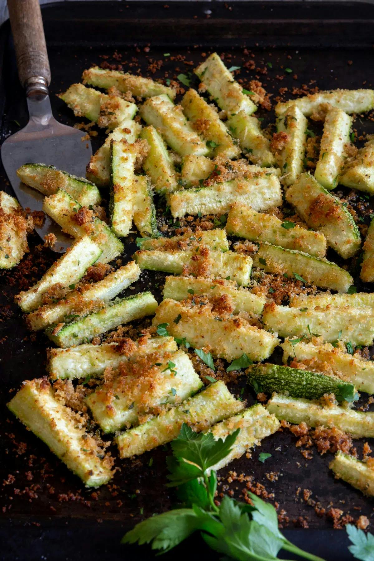 Breaded baked zucchini on a black cookie sheet.