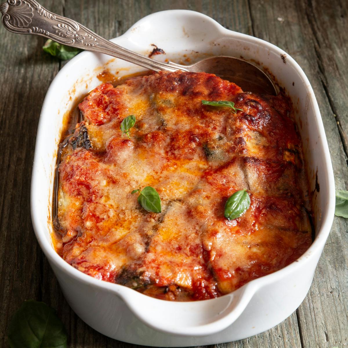 Eggplant mess in a white baking dish with a silver spoon.