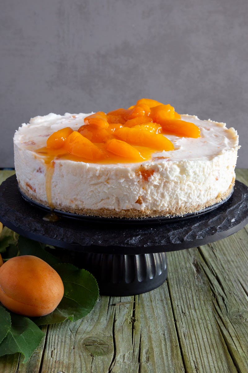 White chocolate apricot cheesecake on a black cake stand.