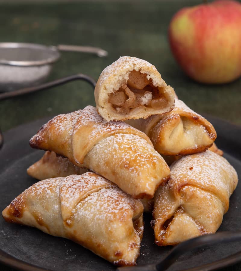Easy apple pie roll ups on a black plate with one cut in half.